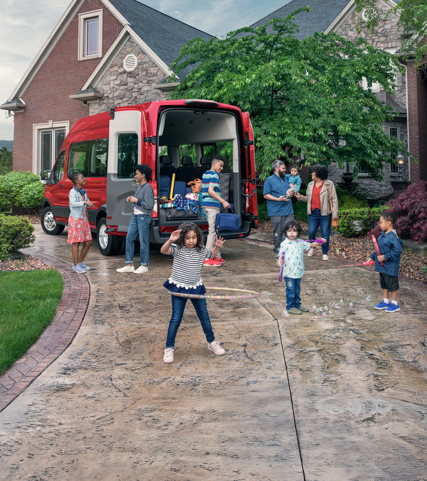 Two parents and a group of children stand behind a red Ford Transit Passenger Van.