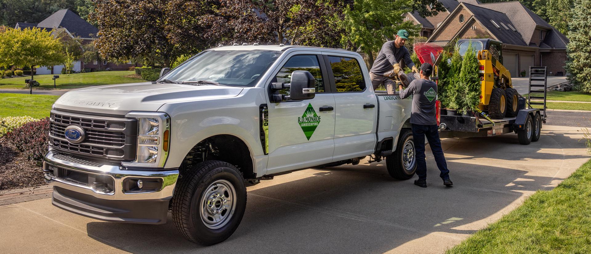 2026 Super Duty® truck parked in a driveway hitched to a trailer carrying landscaping equipment