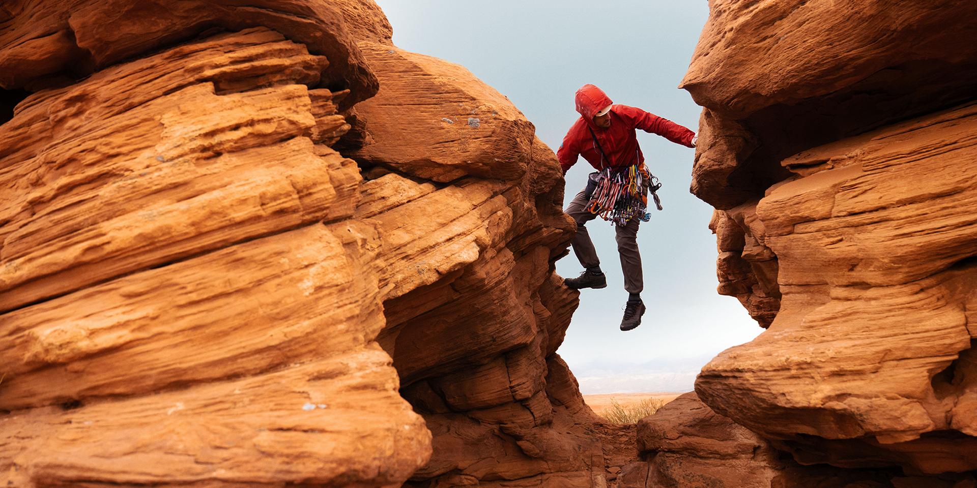 A male rock climber moves upward between two rock faces.