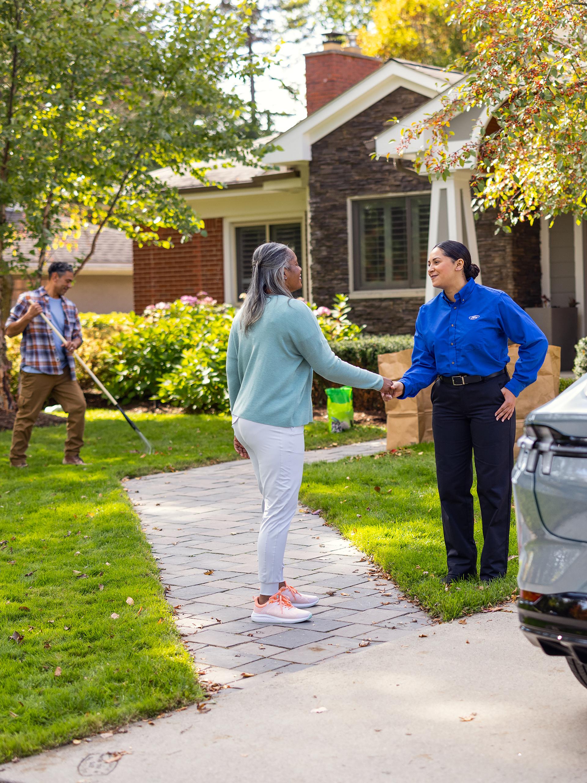 Customer shaking hands with a Ford Service technician next to a Ford vehicle parked in a residential driveway.