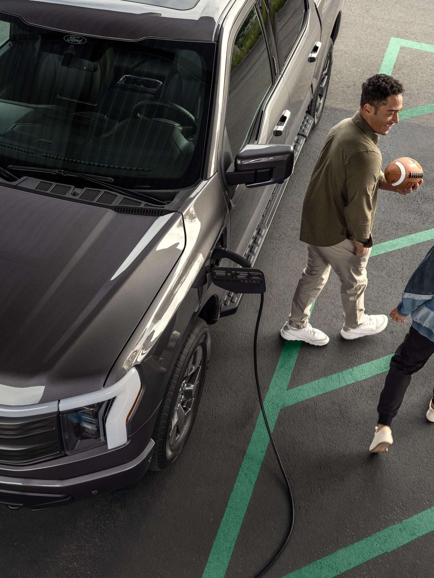 A couple walking away from their Ford F-150 Lightning charging in a parking lot with charging icon overlaid.