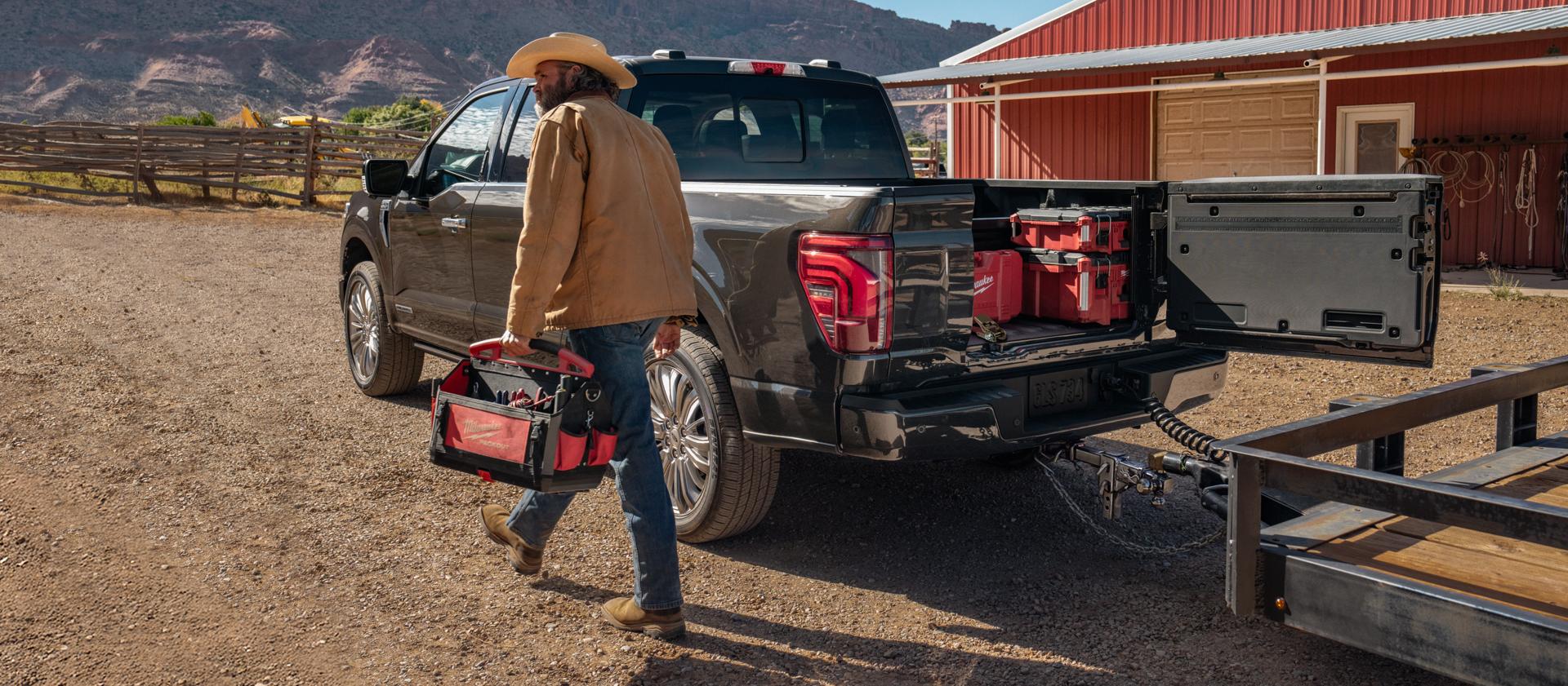 A man walks by an F-150 with a trailer hitched and Pro Access Tailgate open.