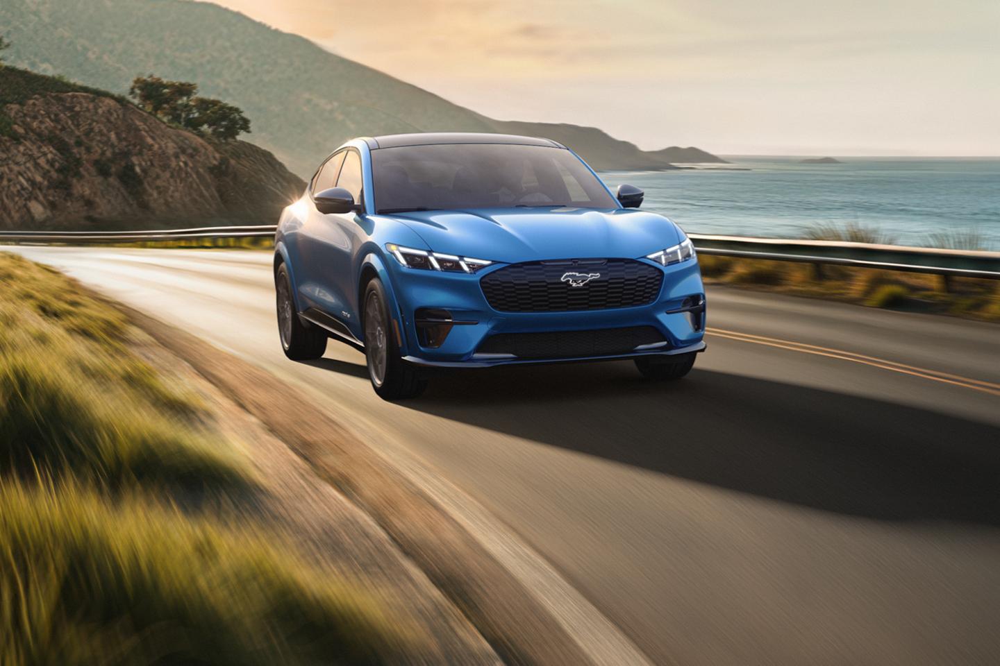 Mustang Mach-E driving on an urban road at sunset.
