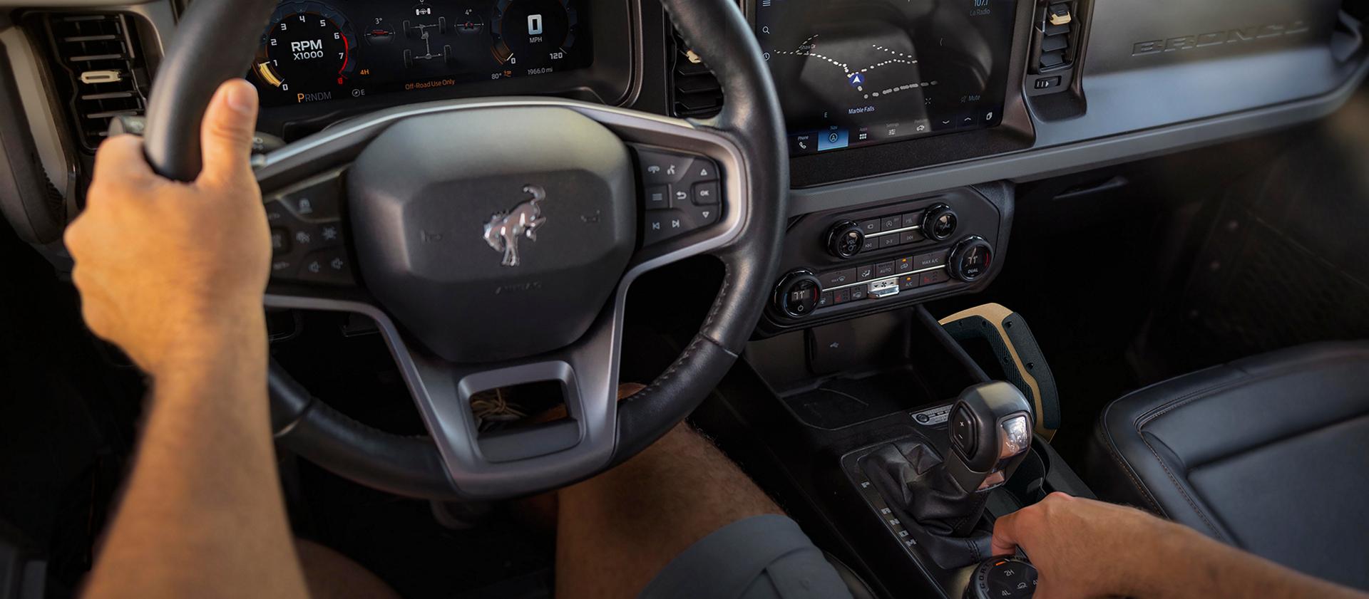 The dashboard of a 2026 Ford Bronco® SUV, with a driver's hands visible on the wheel and drive mode selector