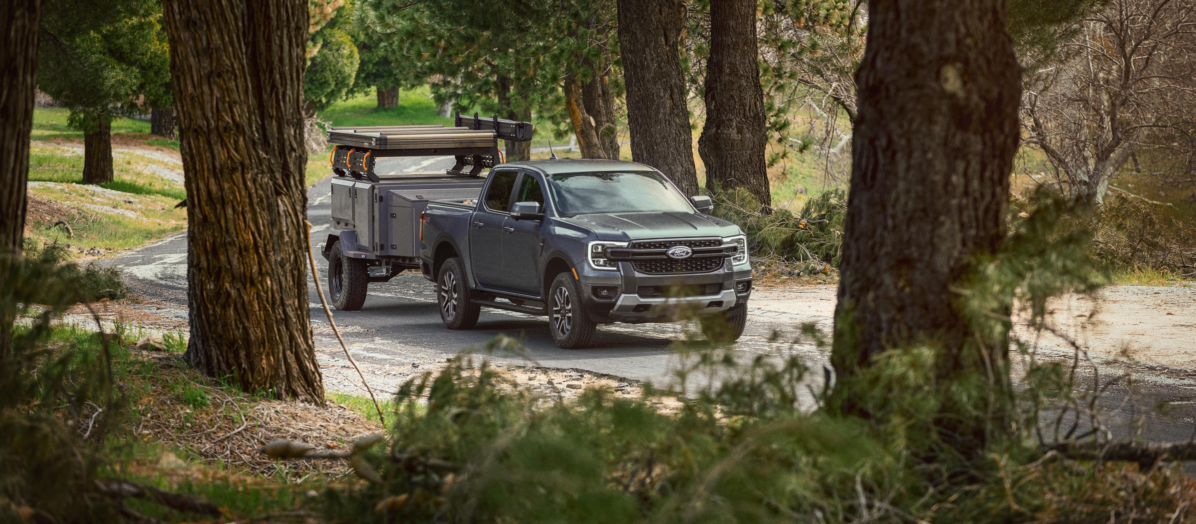A grey 2025 Ford Ranger® towing a trailer through a wooded road