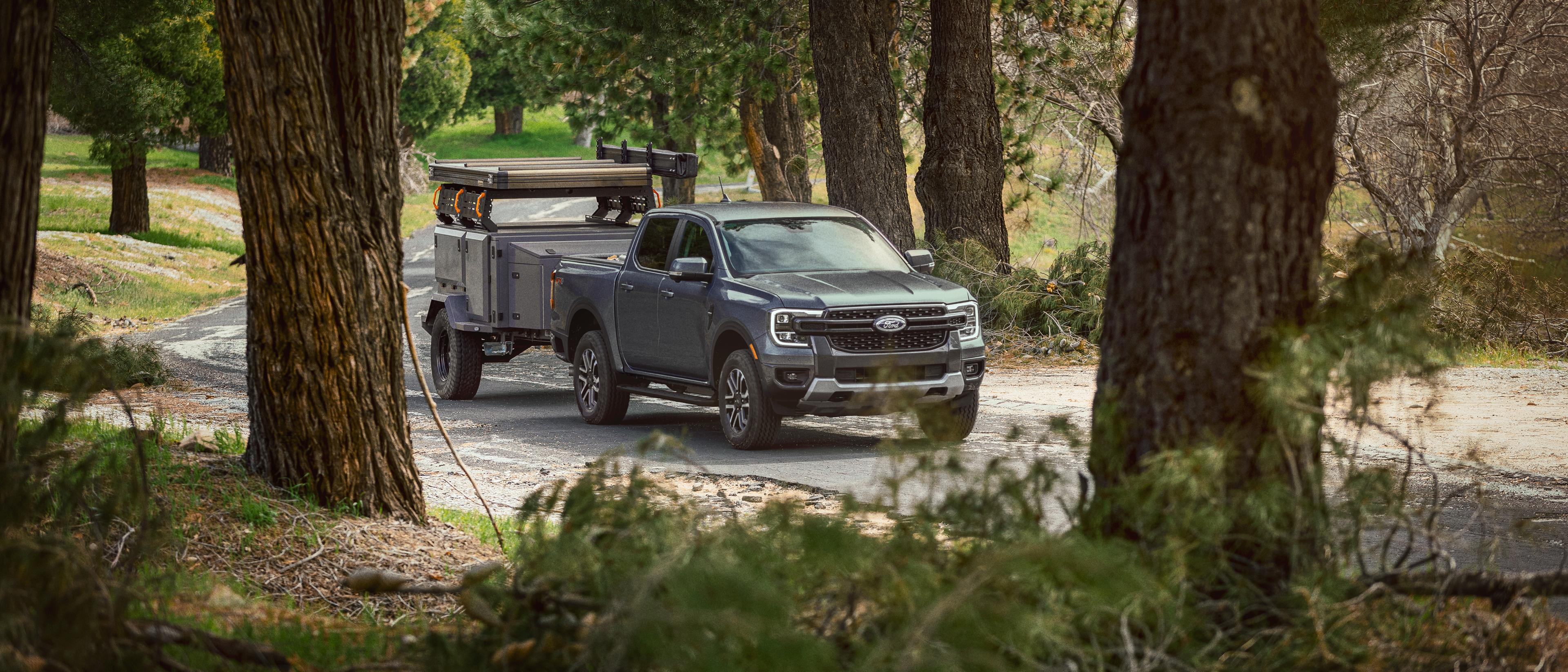 A carbonized grey 2025 Ford Ranger® towing a trailer on a wooded road