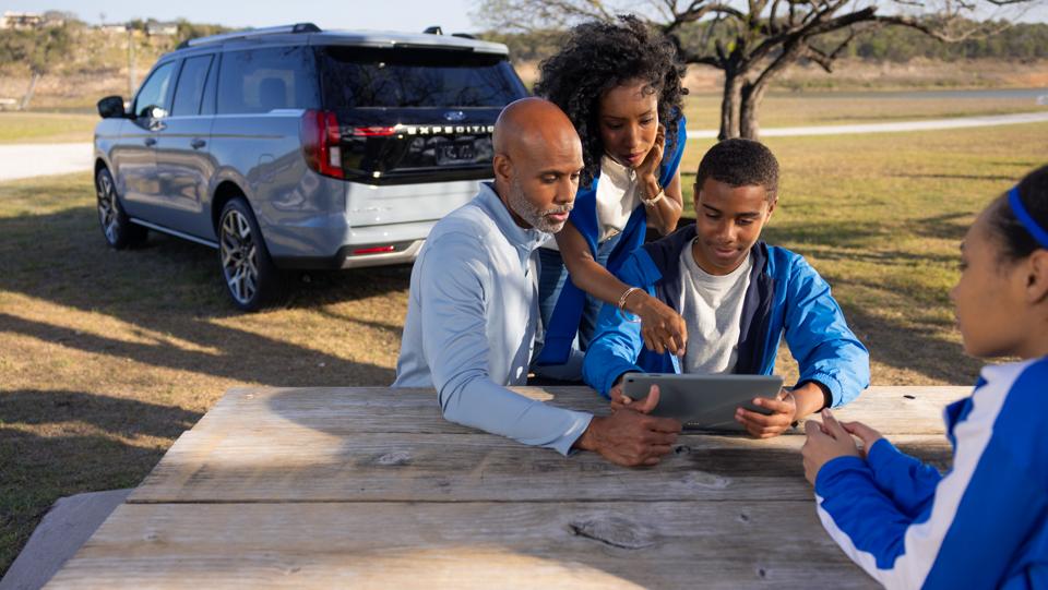 Three people using the Wi-Fi® hotspot with a parked 2026 Ford Expedition® SUV in the background