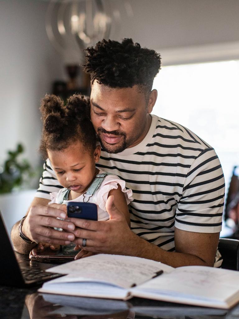 A man holds his child in his lap while interacting with the Ford app on his phone