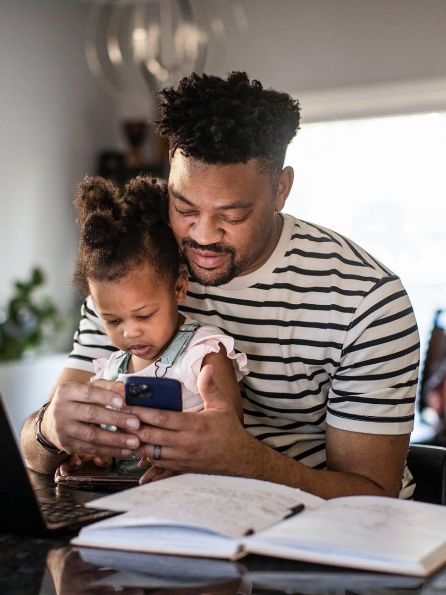 A man holds his child in his lap while interacting with the Ford app on his phone