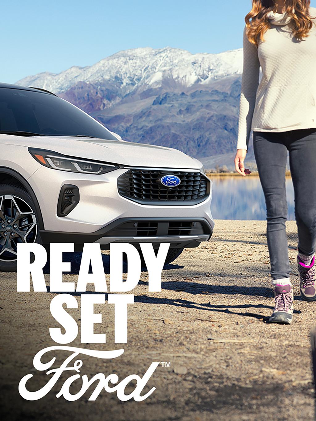 A white Ford Escape parked with mountains in the background and two women walking