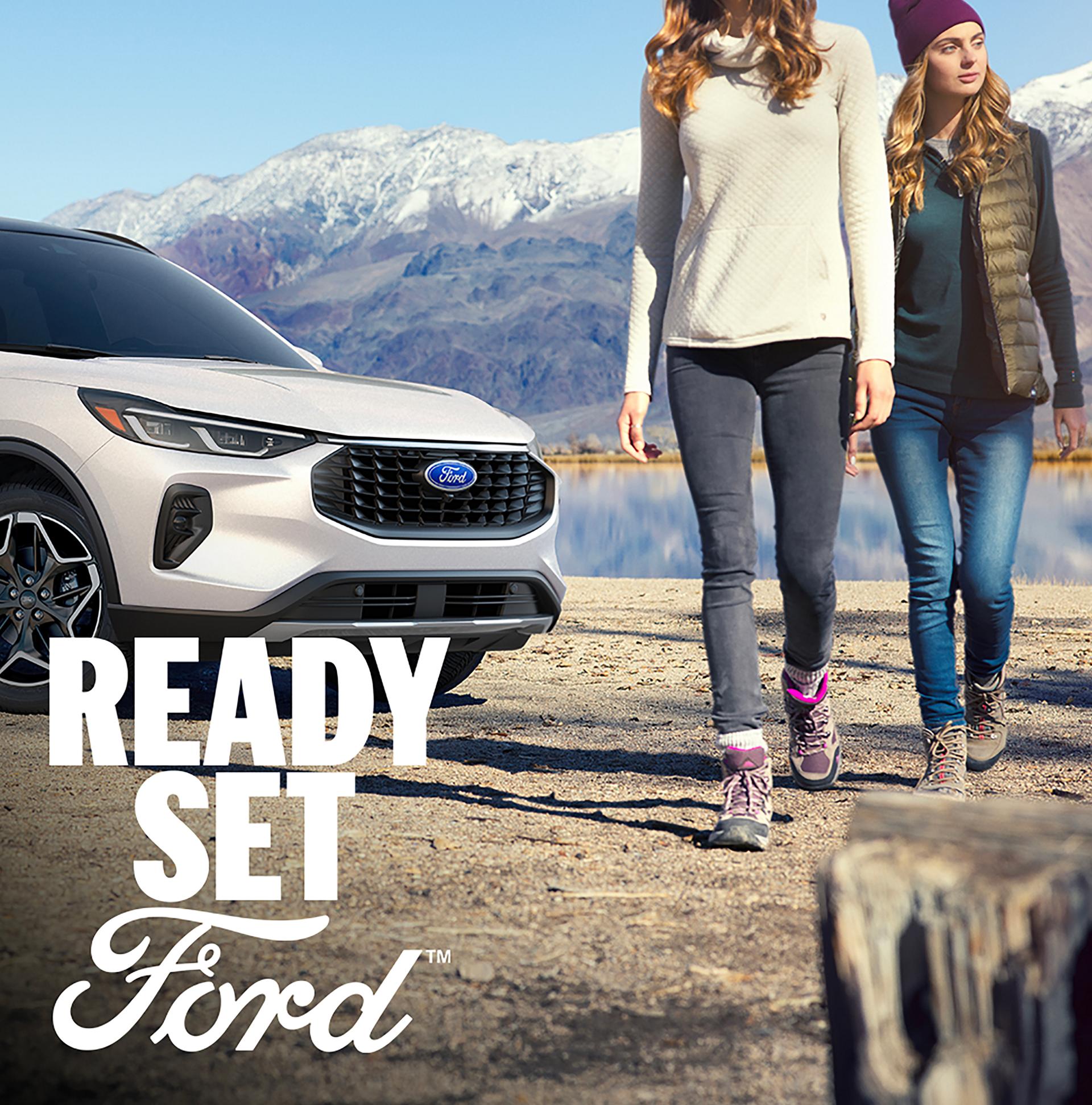 A white Ford Escape parked with mountains in the background and two women walking