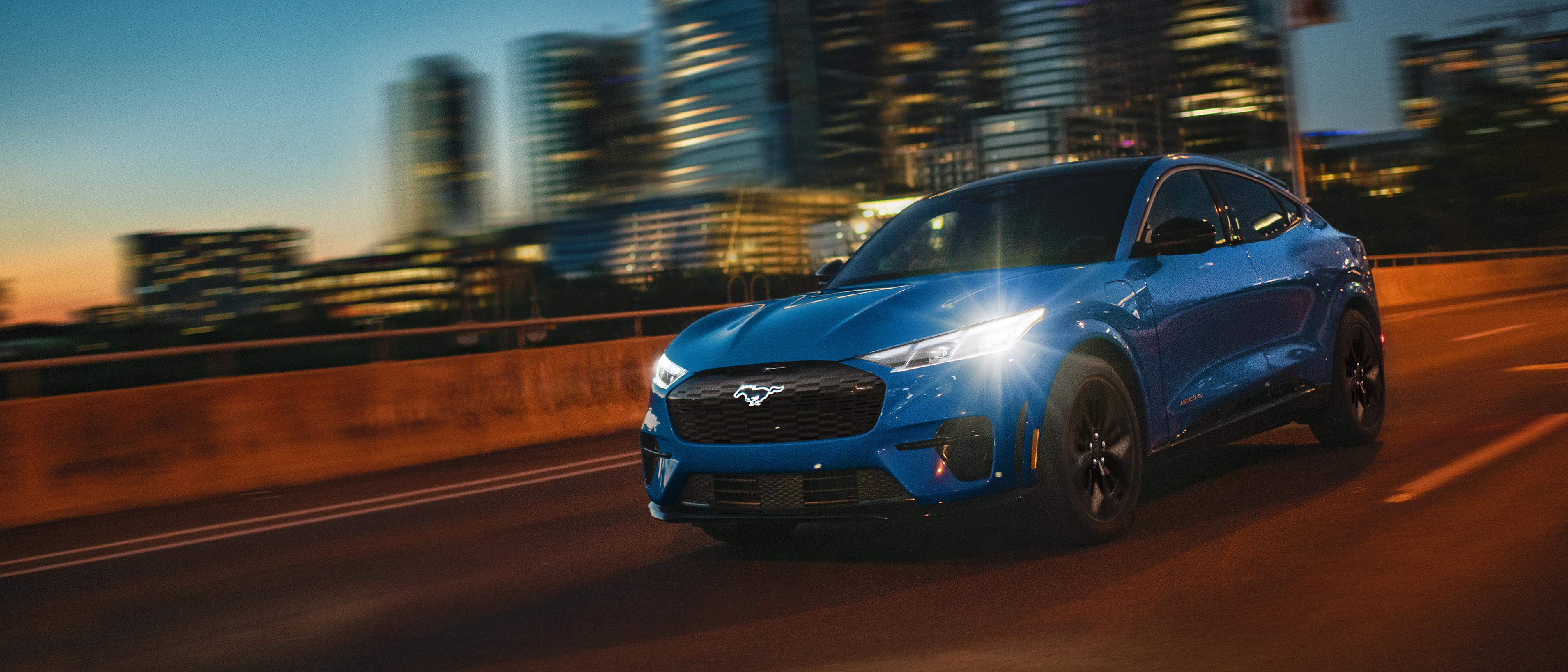 2025 Ford Mustang Mach-E® being driven on a freeway at night with city lights augmented by lens flares