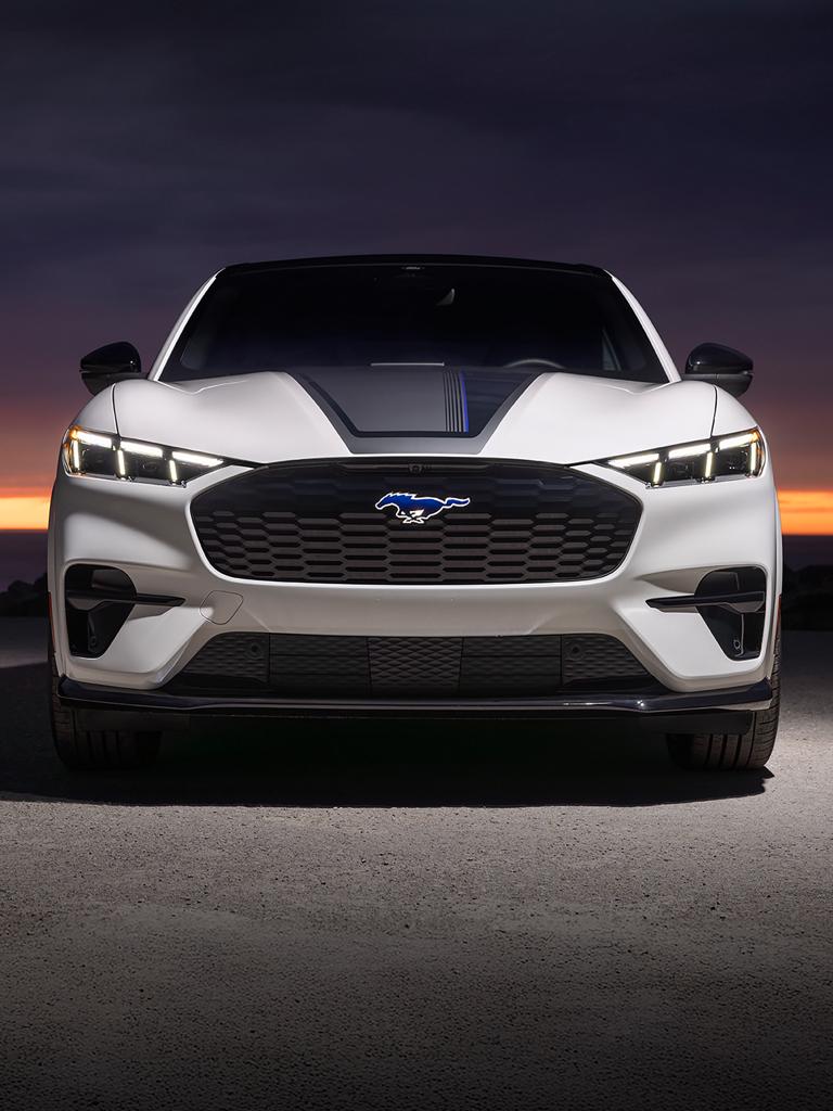 Front end of a 2026 Ford Mustang Mach-E® GT model with hood stripe against a sunset background