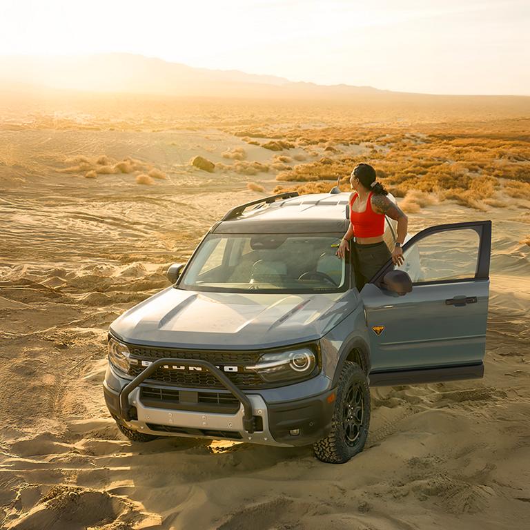 A 2026 Ford Bronco Sport® SUV parked in the desert with a person standing on the door sill of the vehicle