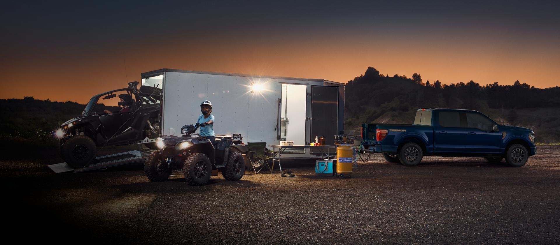 2025 Ford F-150® Tremor® truck powers an air compressor using Pro Power Onboard™ parked near a brightly lit ATV trailer