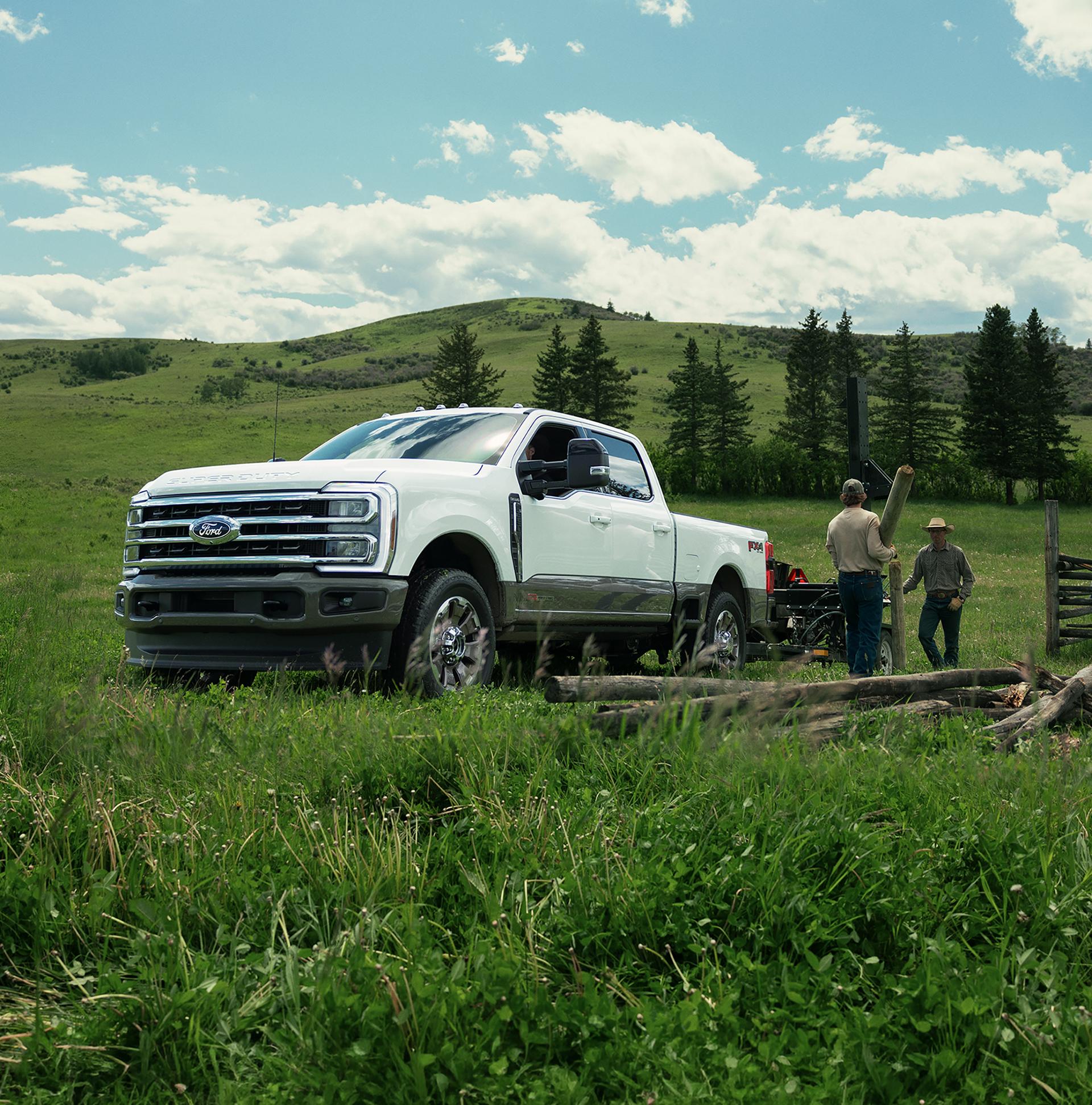 2027 Ford Super Duty® F-350® King Ranch® model towing a trailer of lumber with two workers unloading the lumber from the trailer