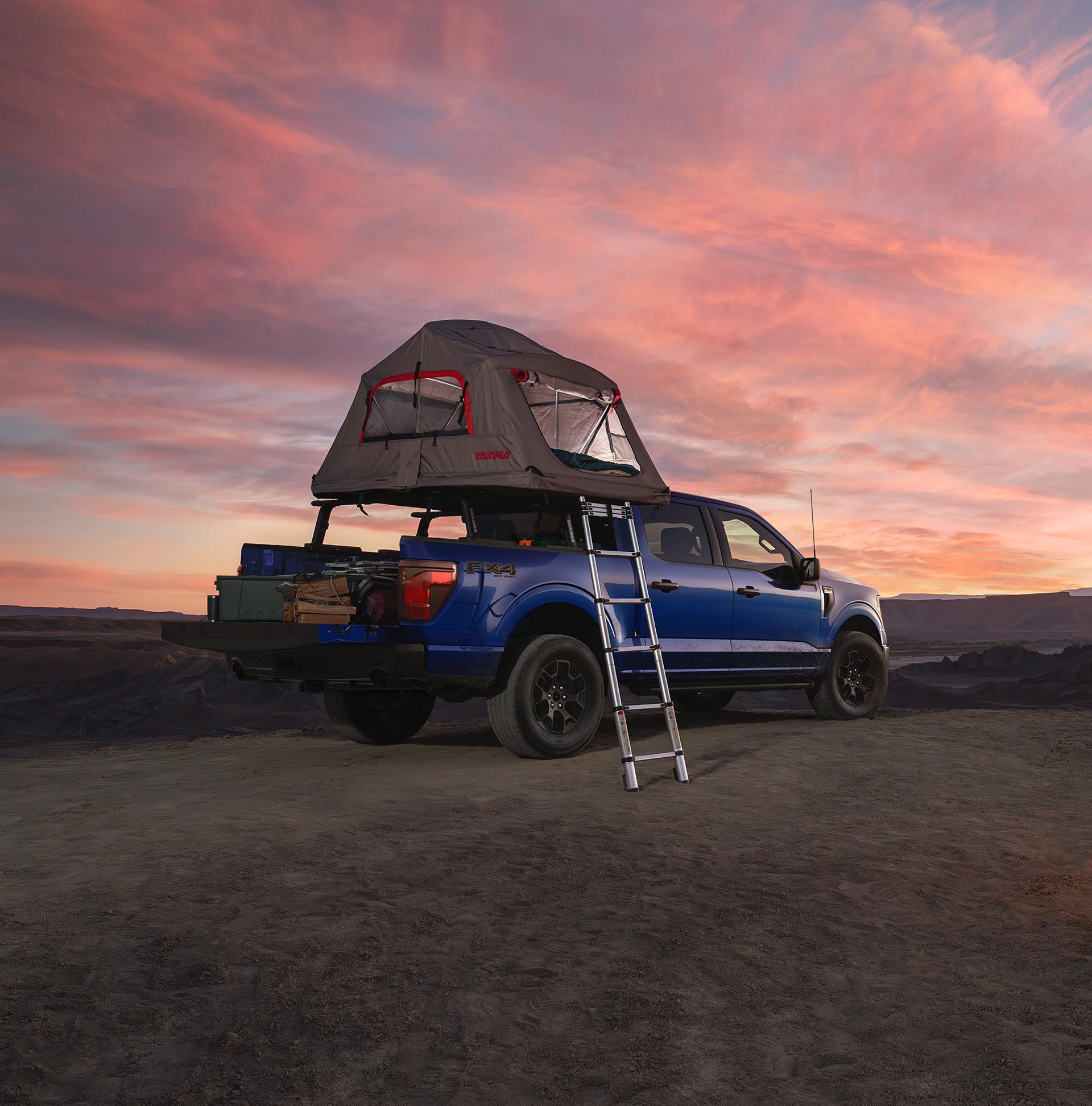 Man starting a campfire near a parked 2026 Ford F-150® STX® FX4 model with a Ford Accessories tent at dusk