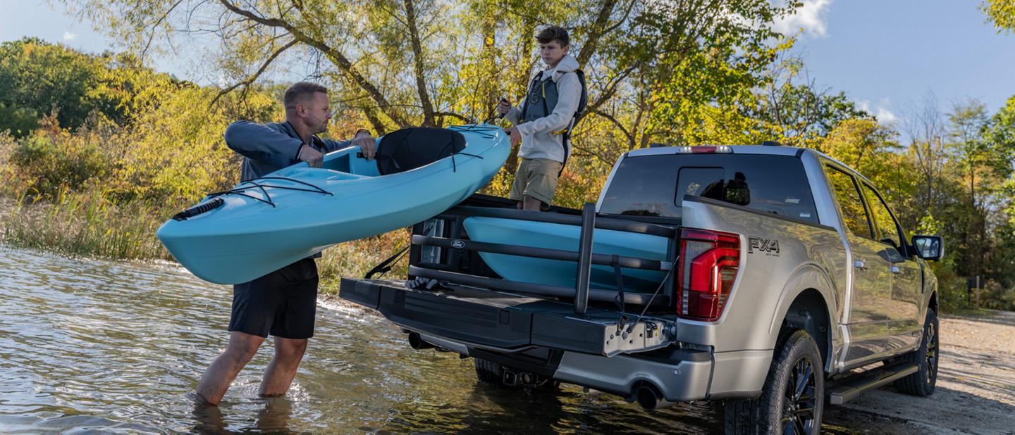 Two people unload a canoe from the bed of an F-150 parked at water’s edge.