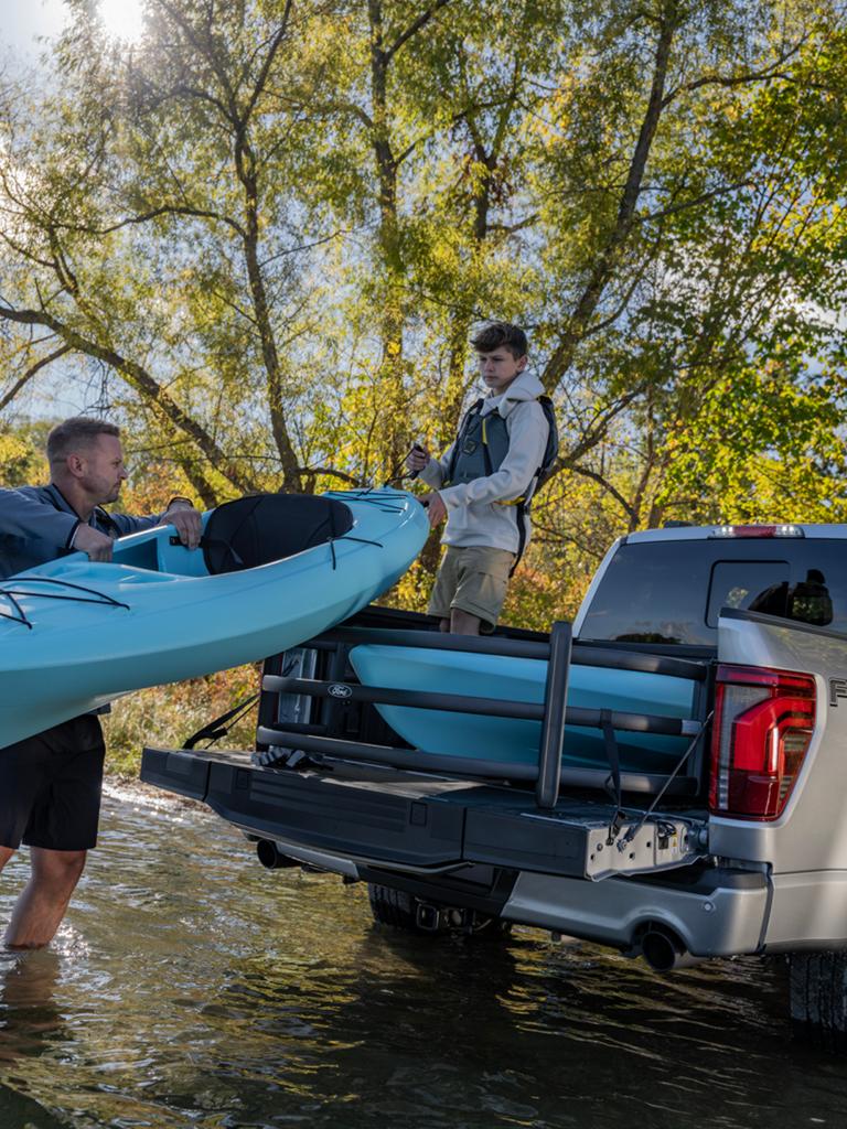 Two people unload a canoe from the bed of an F-150 parked at water’s edge.