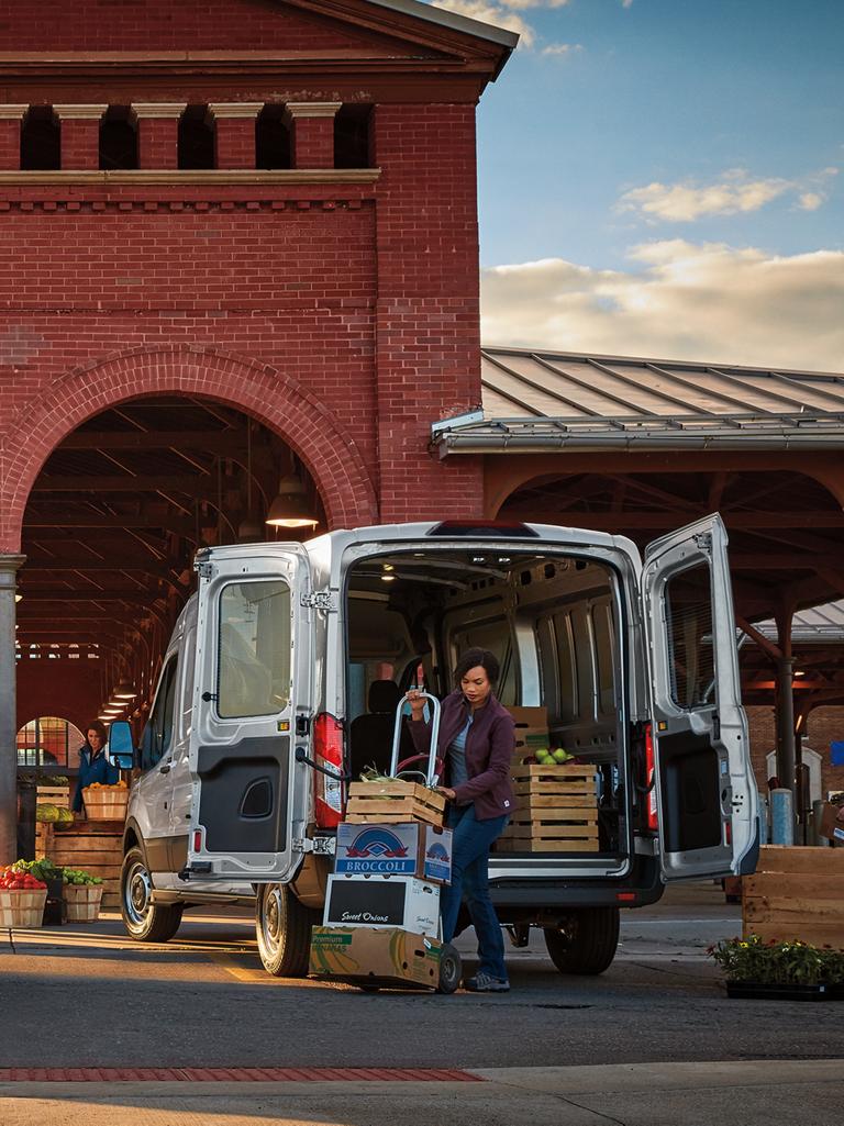 Two white 2027 Ford Transit® Cargo Vans being loaded with fresh produce at an outdoor market
