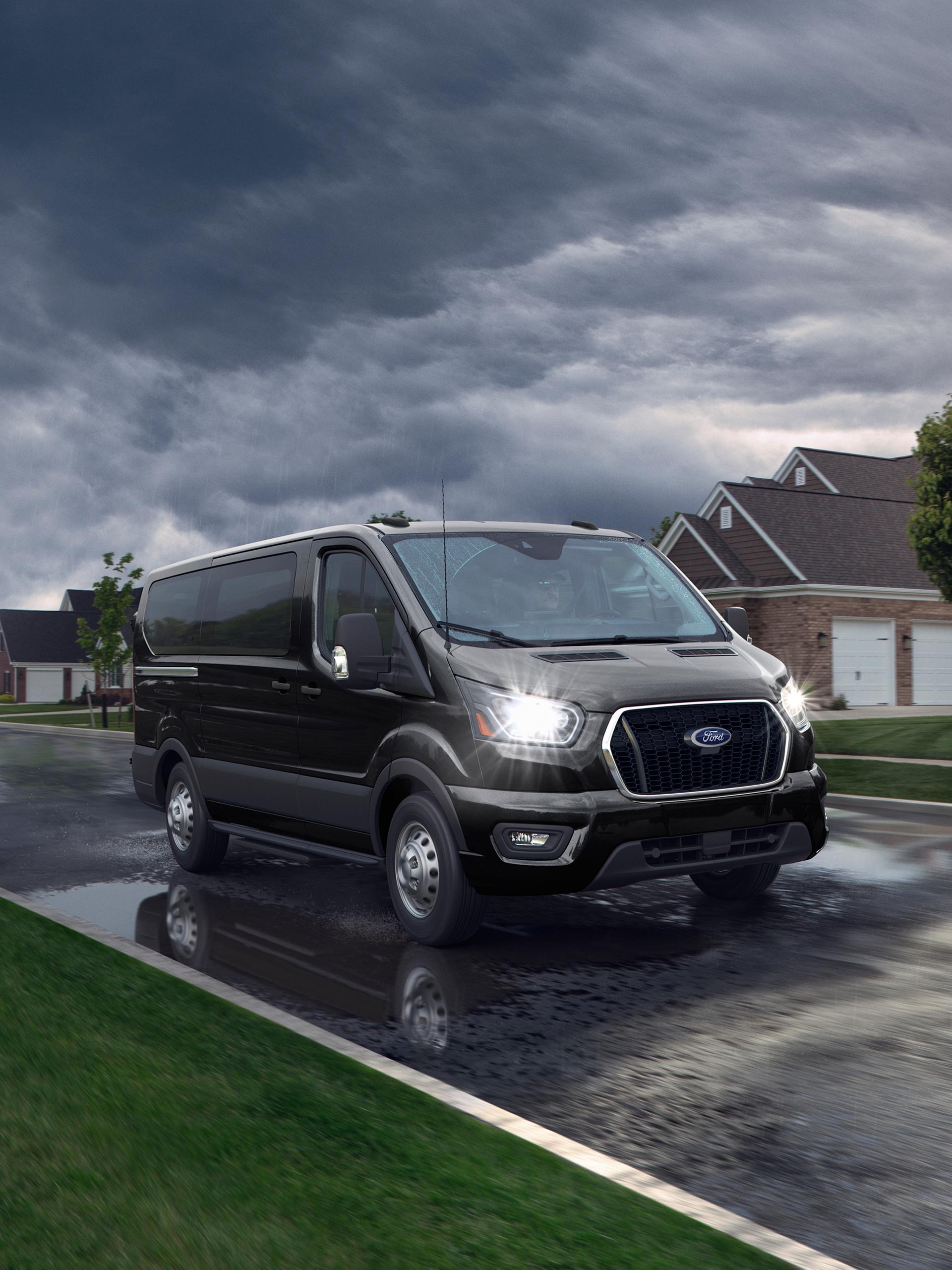 Black 2027 Ford Transit® Van on a wet street with stormy clouds and houses in the background