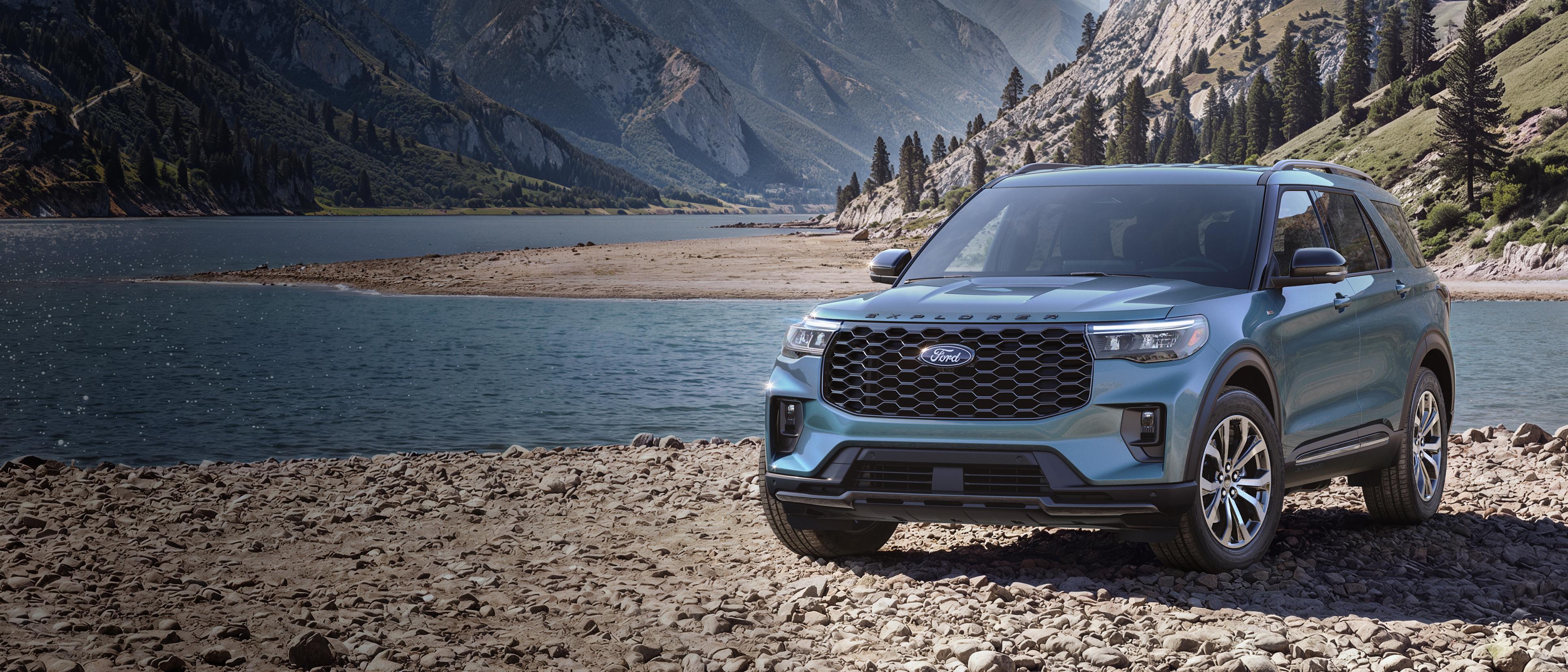 A 2027 Ford Explorer® ST-Line model parked on a rocky expanse near a mountain lake
