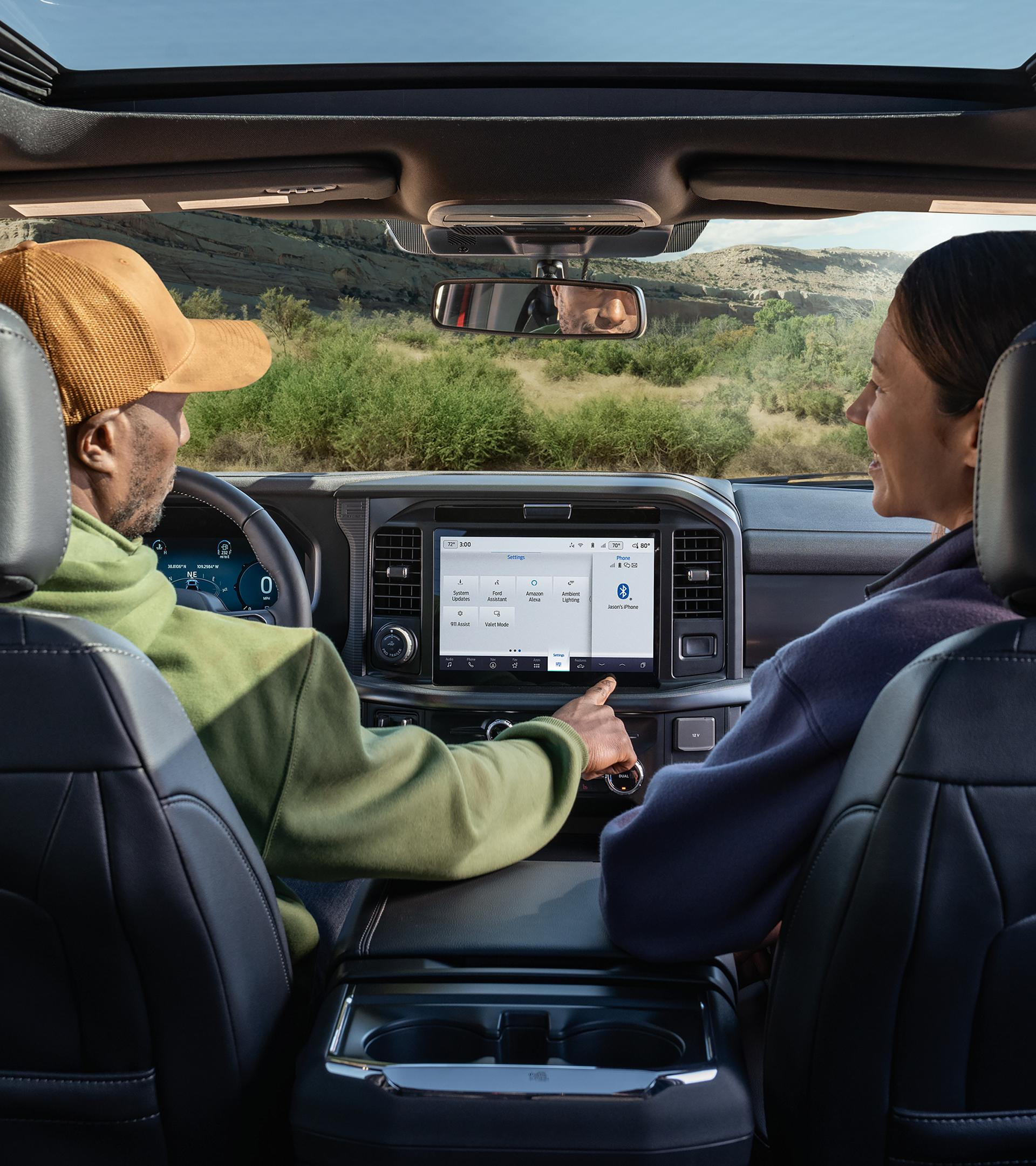 Man using the push-button features on the 12-inch centre display with a woman seated in the passenger seat