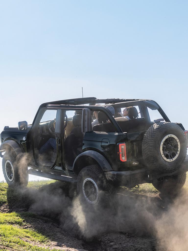 A 2026 Ford Bronco® SUV being driven on a muddy hillside with doors and roof removed