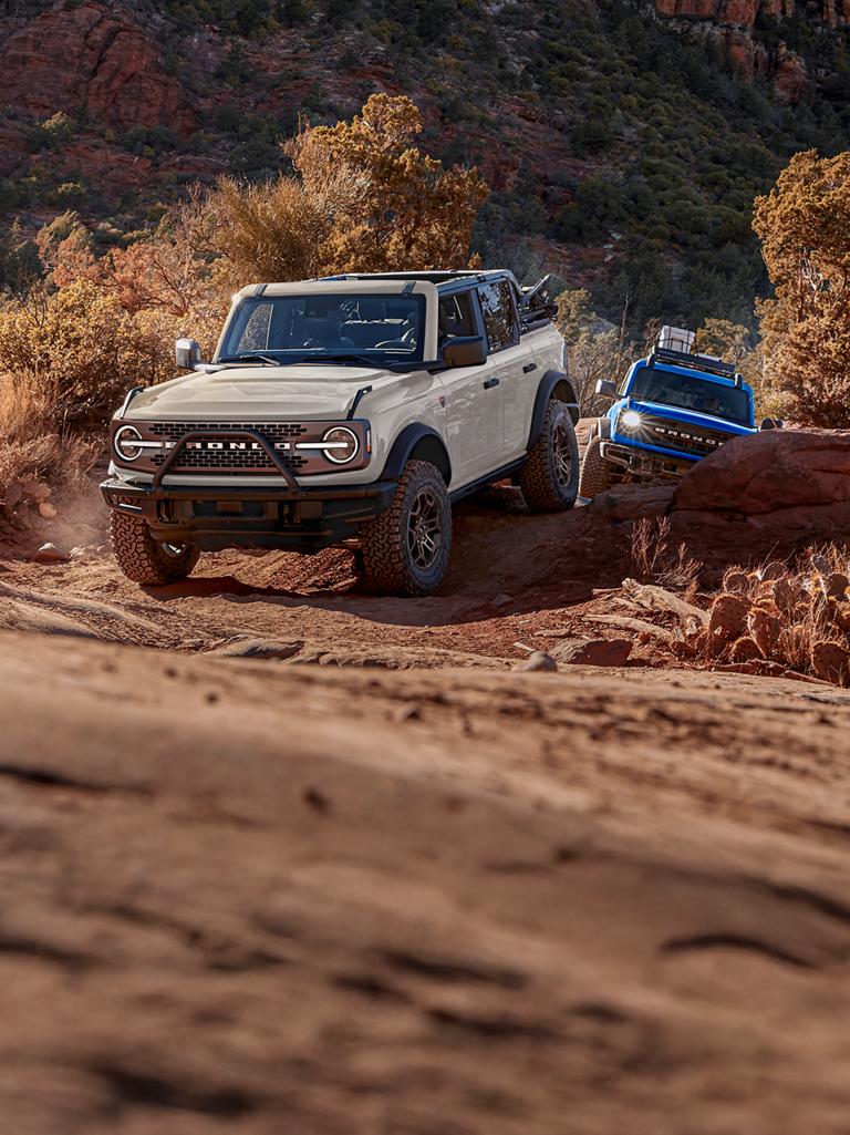 Two 2026 Ford Bronco® SUVs being driven out of a canyon trail
