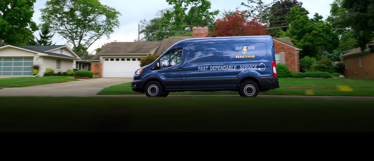 A Blue 2027 Ford Transit® Van drives past houses in a suburban neighbourhood