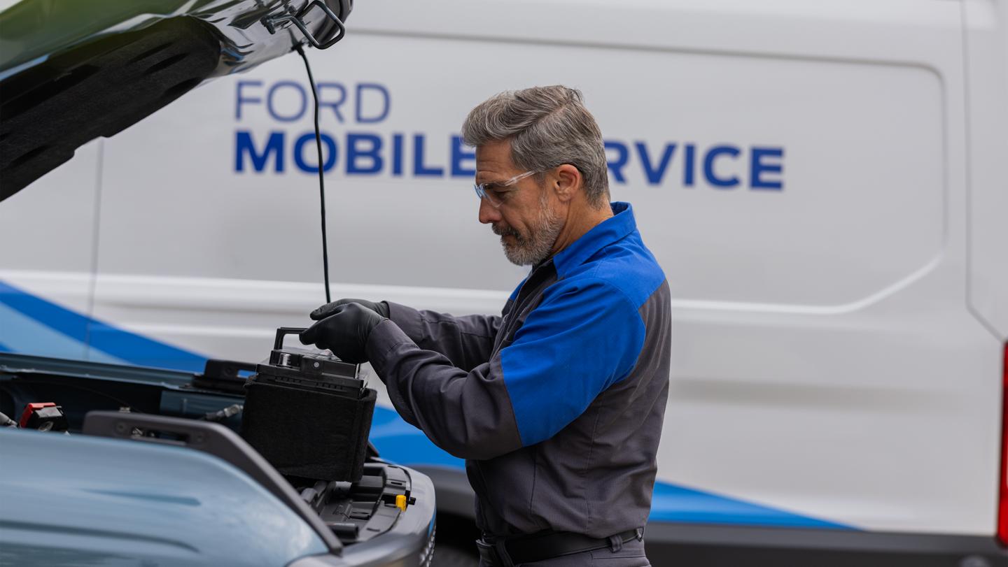 A Ford Service technician changes a windshield wiper on a Ford vehicle. The Mobile Service work truck is in the background.