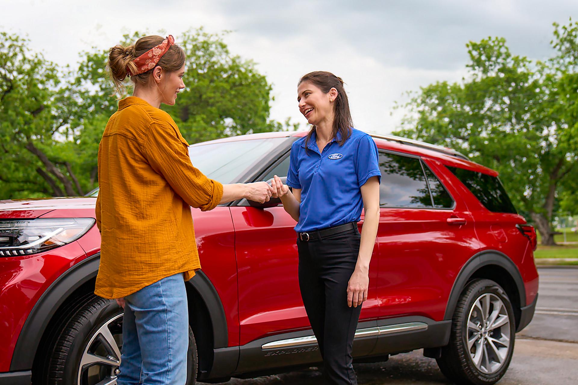A Ford Service employee hands keys to a customer while they stand beside a Ford vehicle.