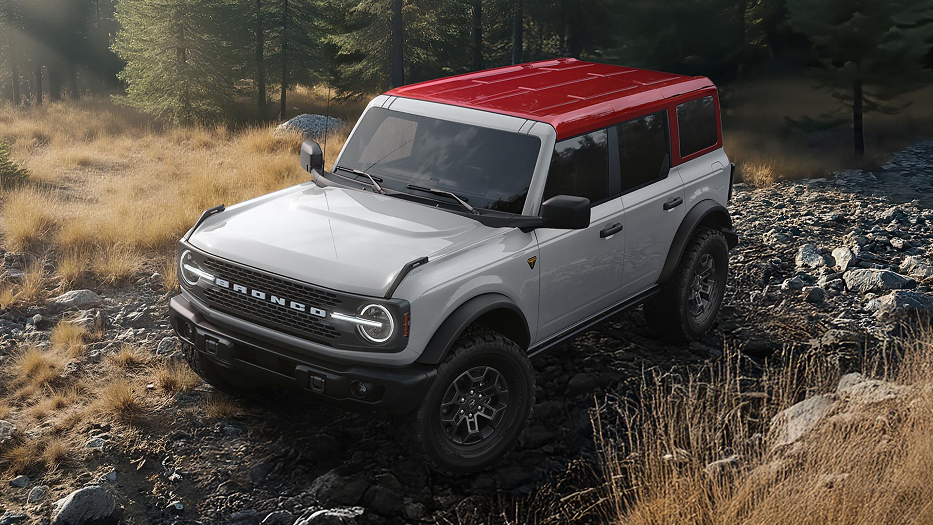 A 2026 Ford Bronco® SUV on a muddy path, with a Avalanche Gray body and a red roof