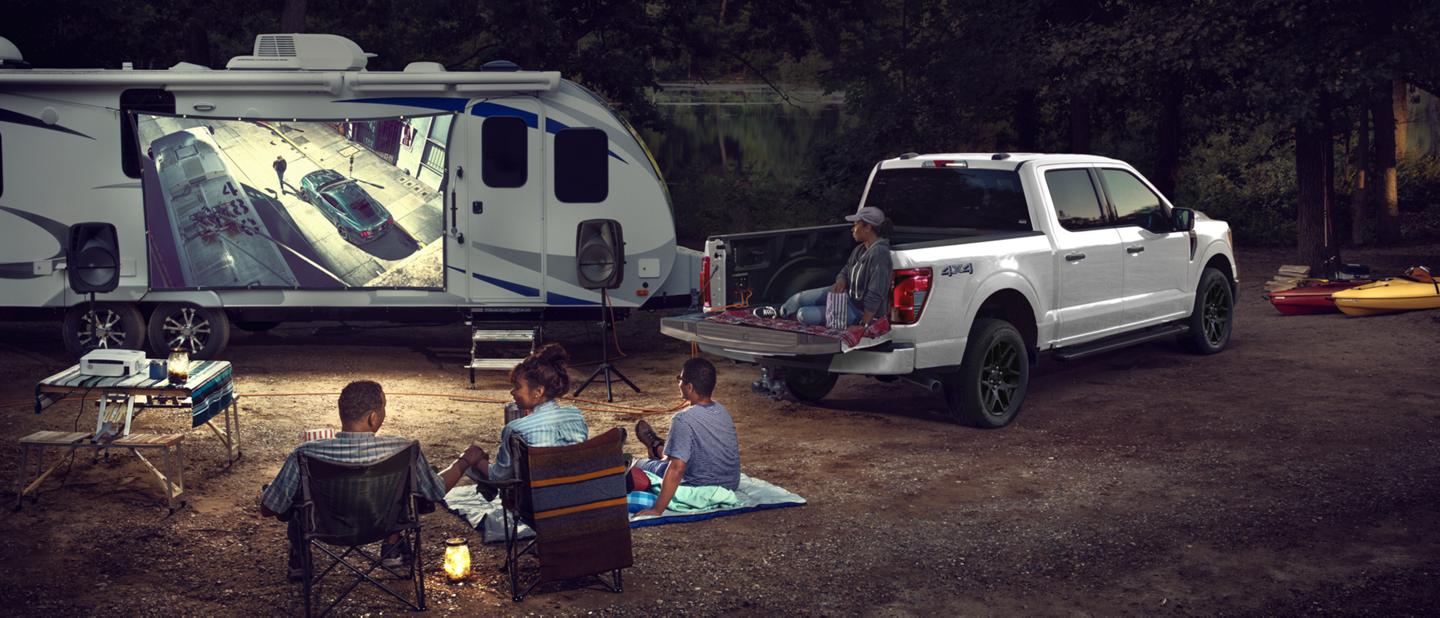 A family at a campsite watching a football match projected onto a trailer parked next to an F-150.