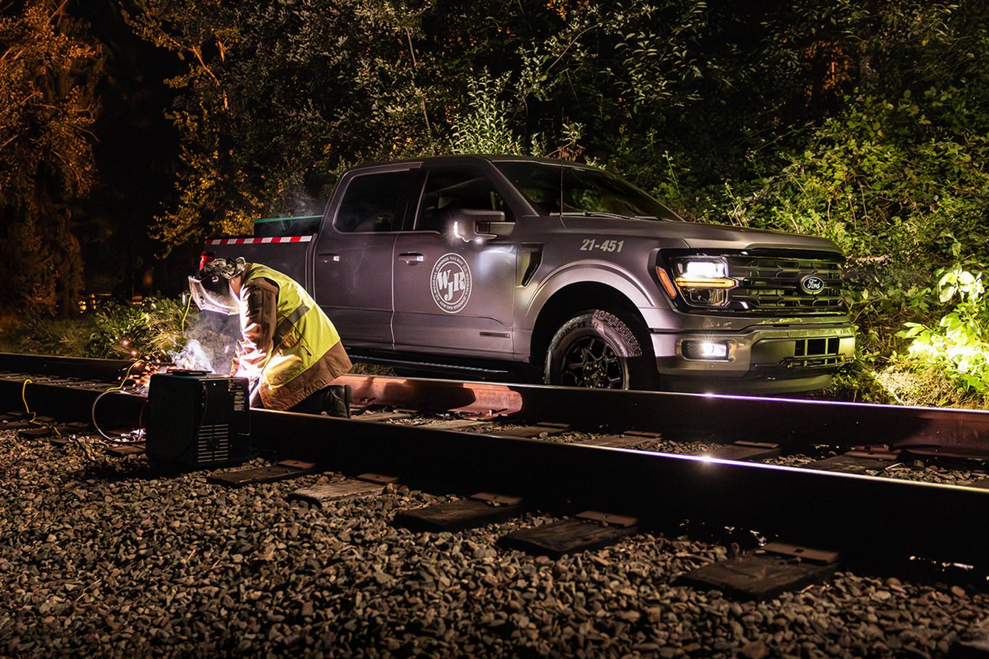 A person welds a railway track at night near a parked F-150.