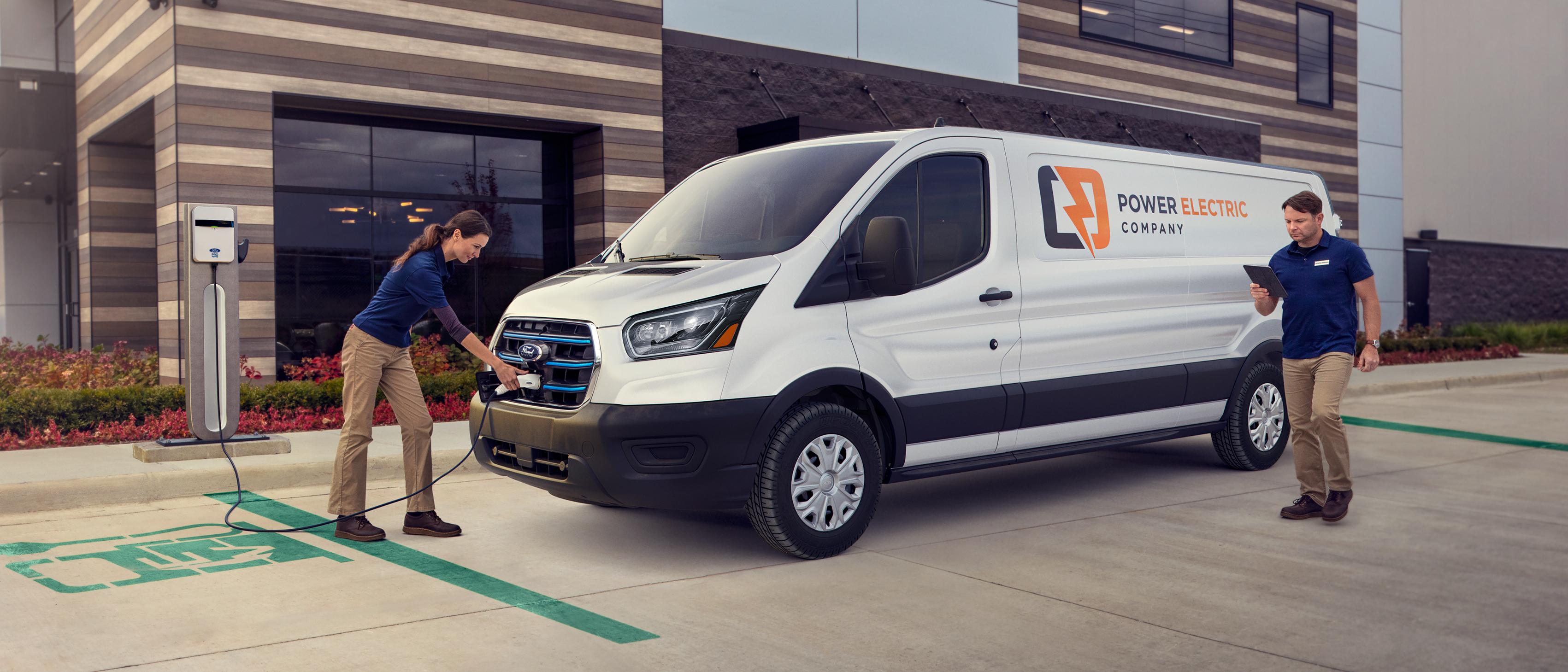 A white 2025 Ford E-Transit™ van parked and being charged by two workers outside a business