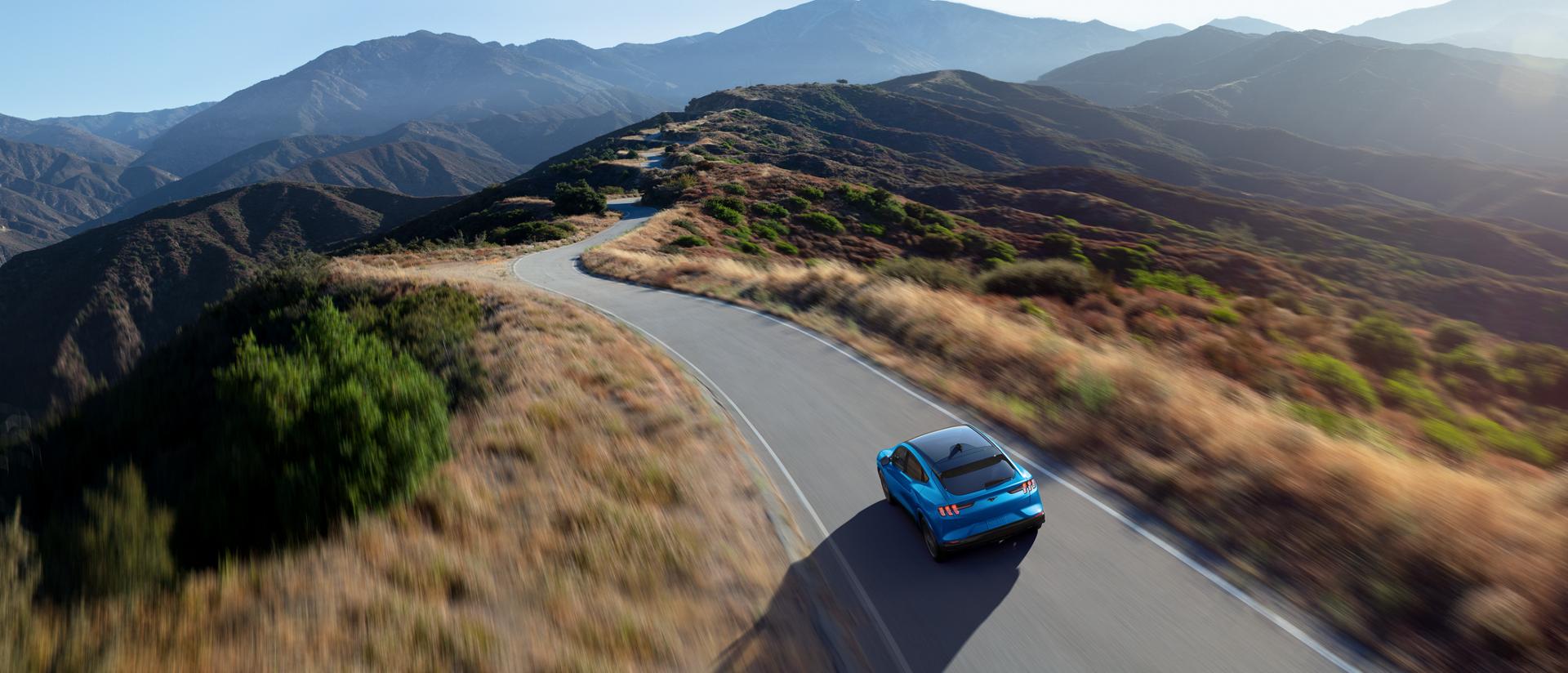 Aerial view of a 2025 Ford Mustang Mach-E® being driven on a scenic road through mountains