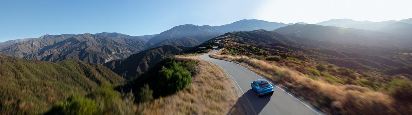 Aerial view of a 2025 Ford Mustang Mach-E® being driven on a scenic road through mountains