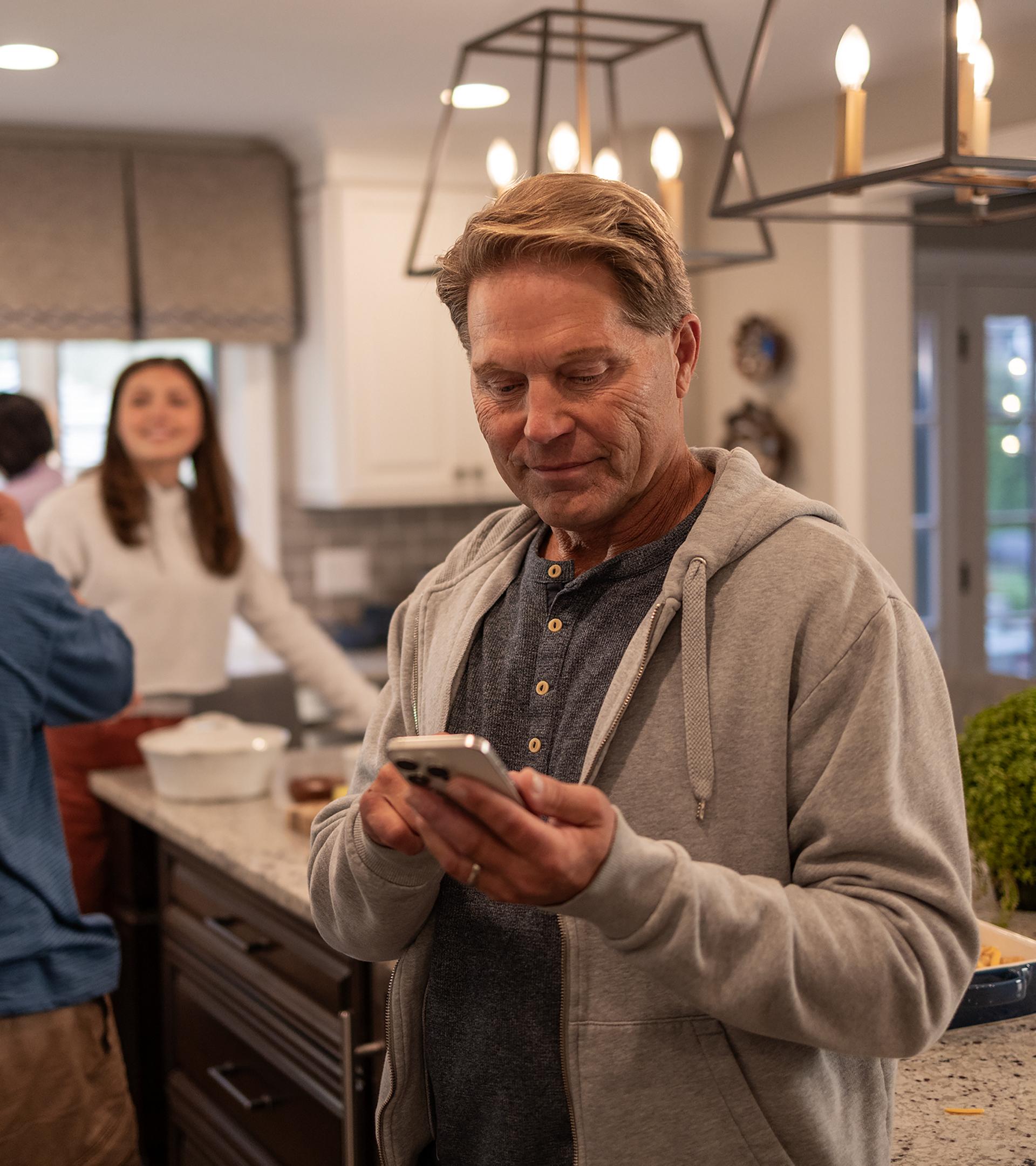 Person standing in a kitchen looking at a smartphone.
