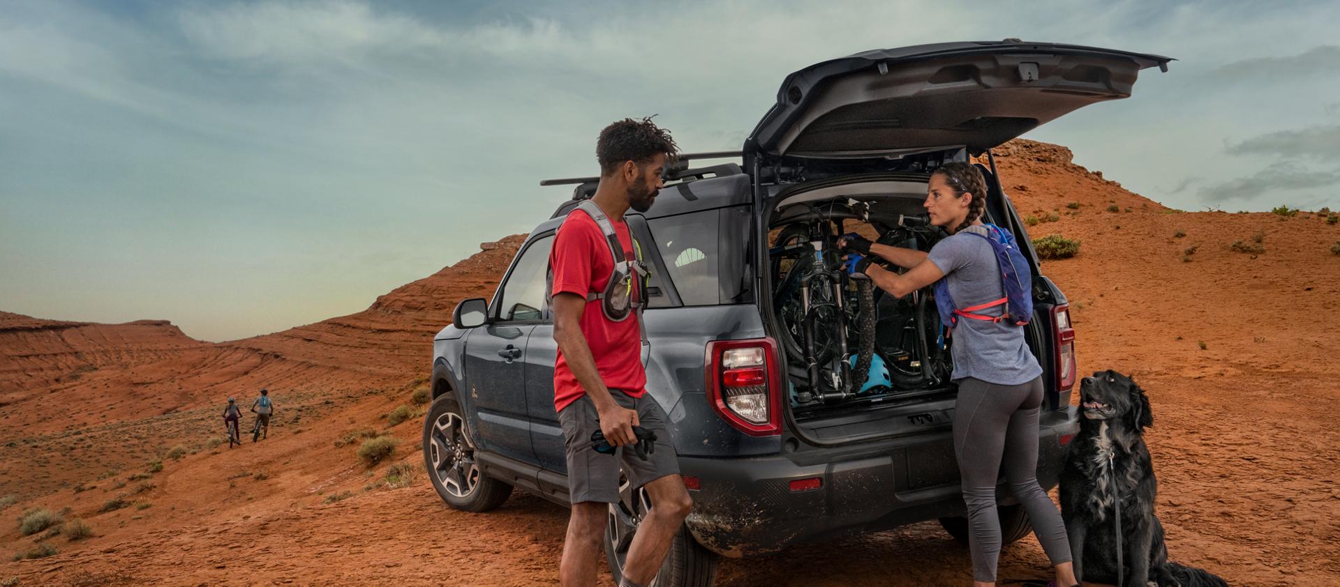 2026 Ford Bronco Sport® SUV parked in the desert with two people standing outside of the vehicle, wearing hiking gear with their dog