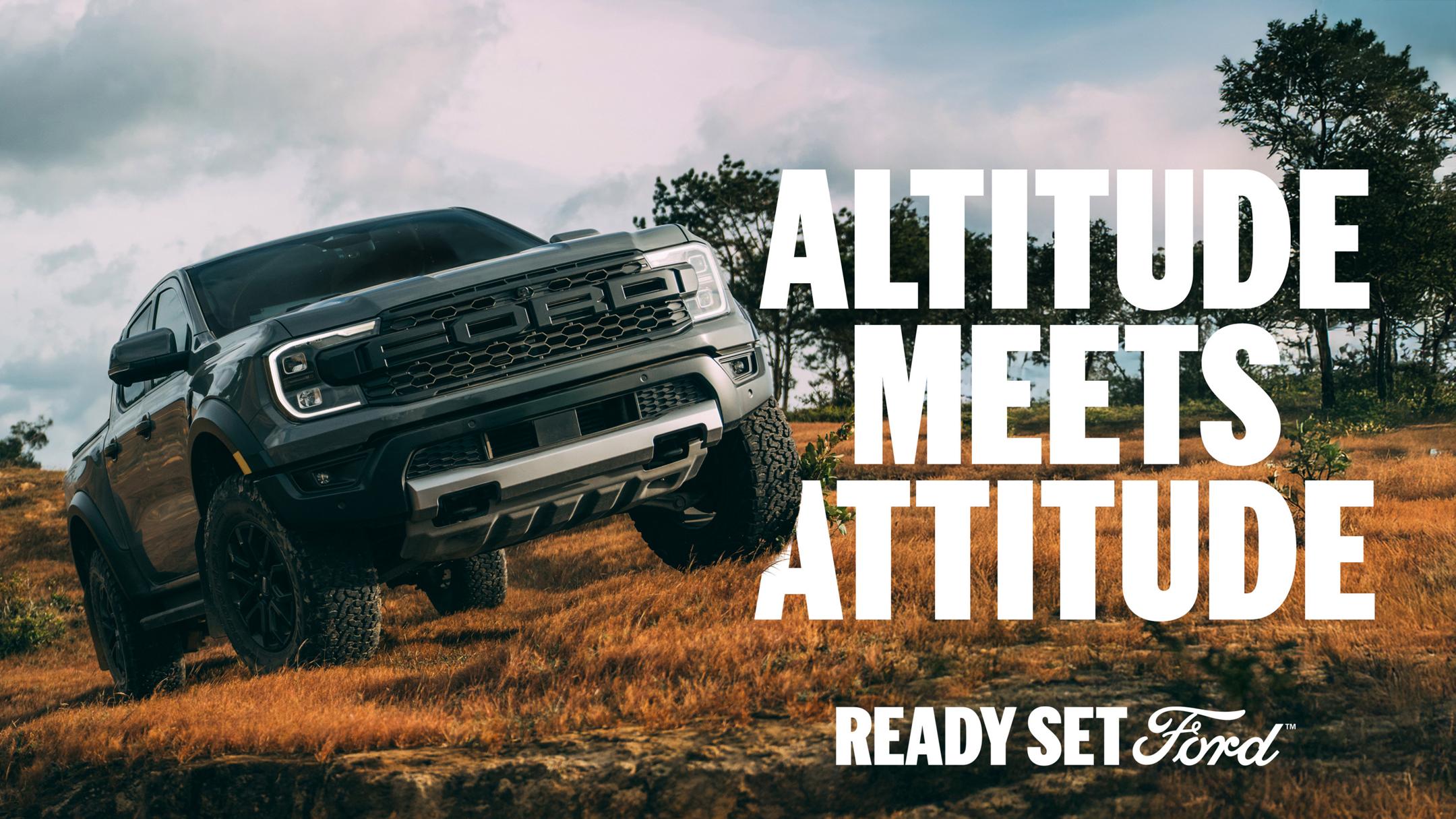 Three-quarter front view of a grey Ford Ranger Raptor off-roading through an open field. White text “Altitude Meets Attitude” appears to the right of the Ranger. In the lower-right corner appears white text “Ready Set Ford”.