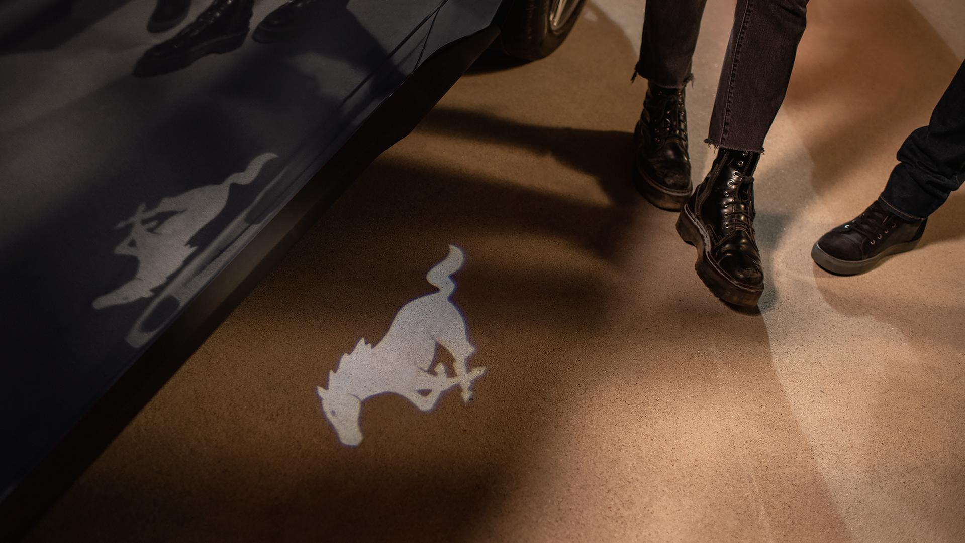Two people standing near a 2026 Ford Mustang® model with available pony puddle lamps
