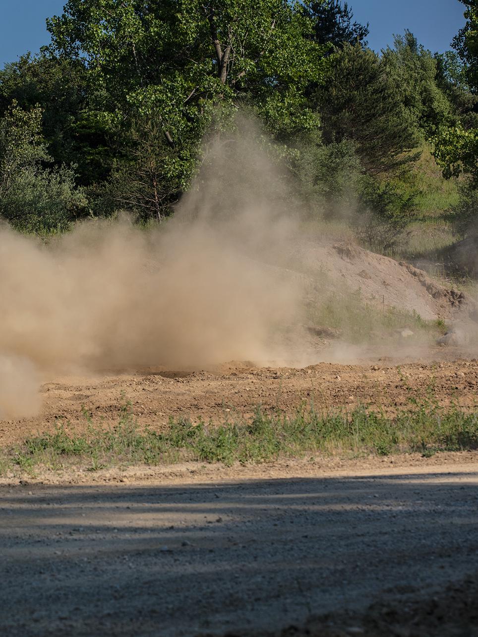 Arid landscape with plumes of sand kicked up by vehicles.