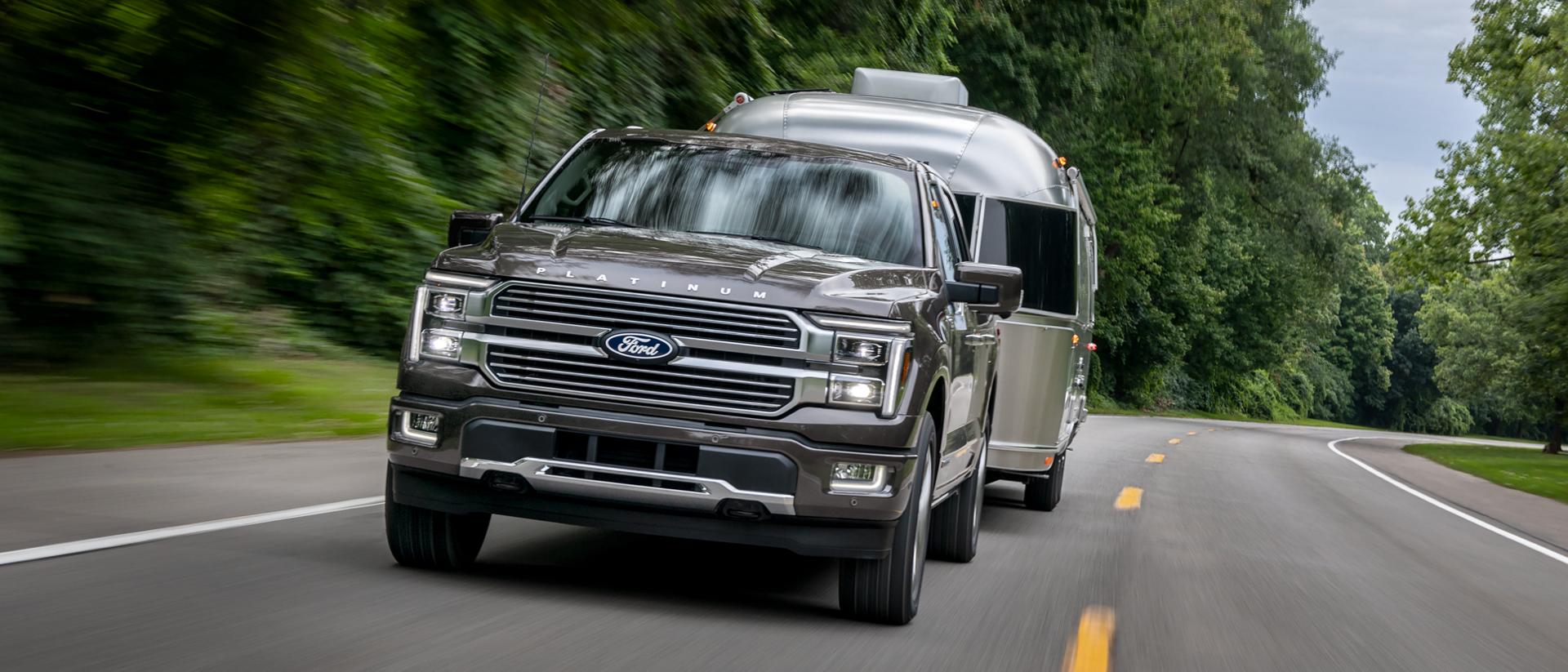 2025 Ford F-150® Platinum® pickup pulling a camper on a tree-lined highway