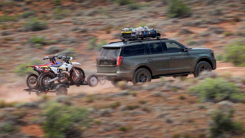 2025 Ford Expedition® Tremor® model with a driver towing a dirt bike trailer on a desert road