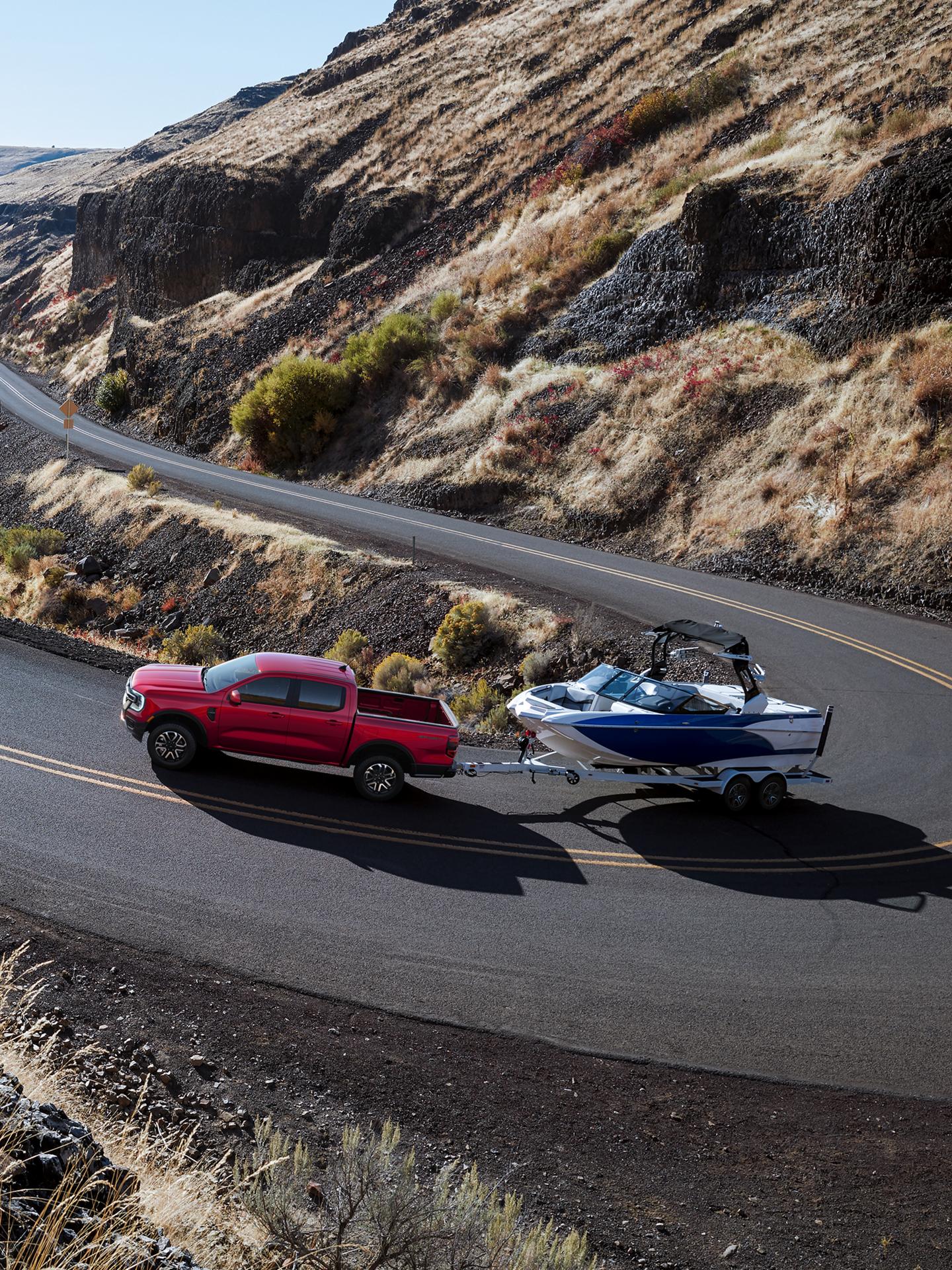 A 2026 Ford Ranger® Raptor® model using the Advanced Towing Package to tow a boat on a winding mountain road