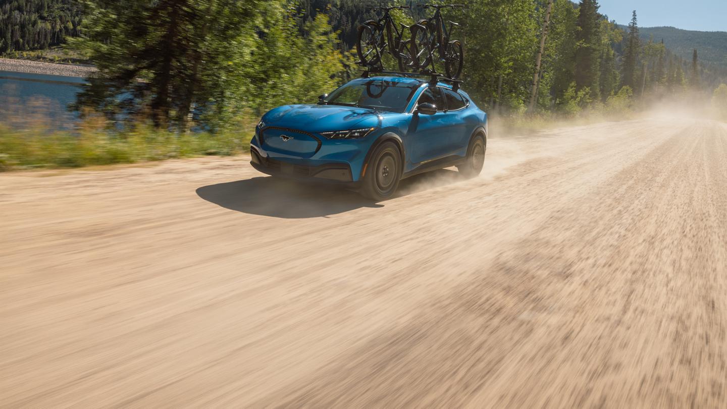 2027 Mustang Mach-E® SUV with optional Trail package and available Ford bike rack accessory being driven on dirt road