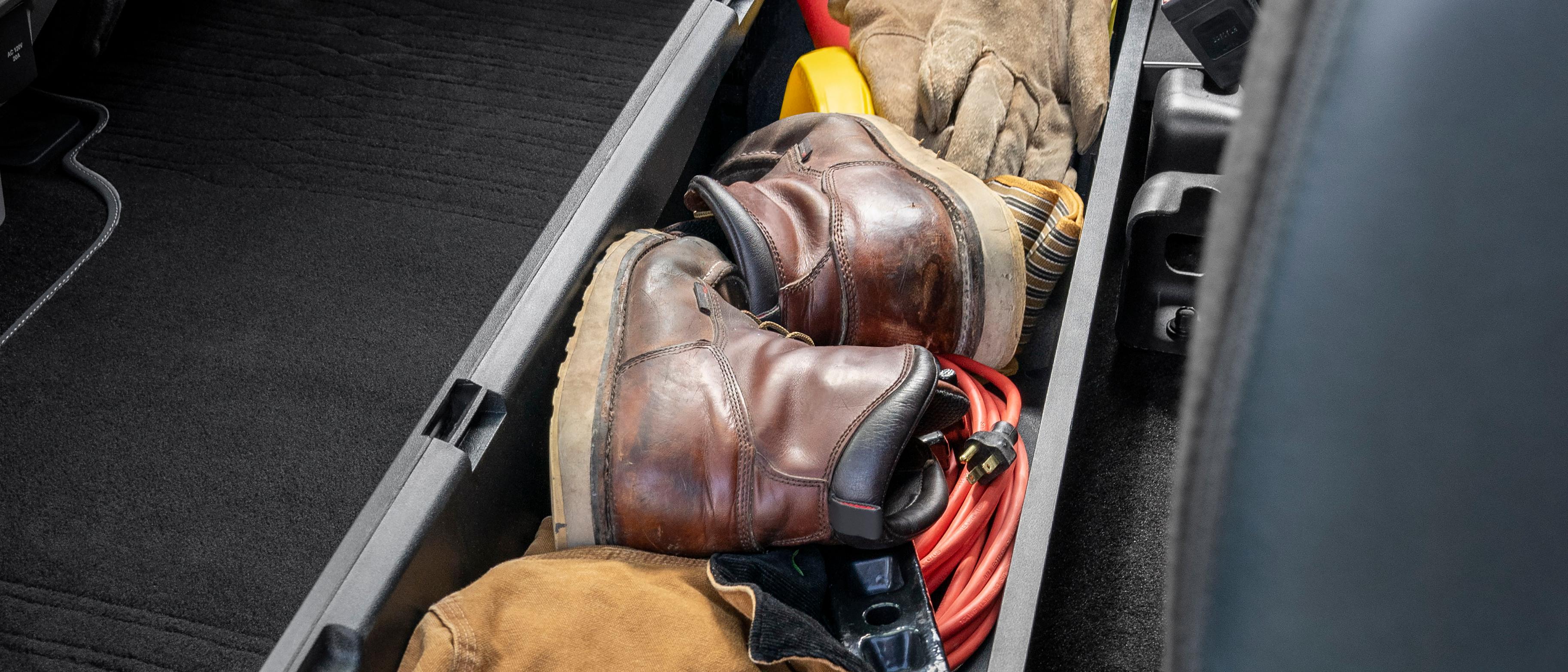 Rear under-seat storage bin pulled out from the seat and filled with leather boots, tools, cables, and gear