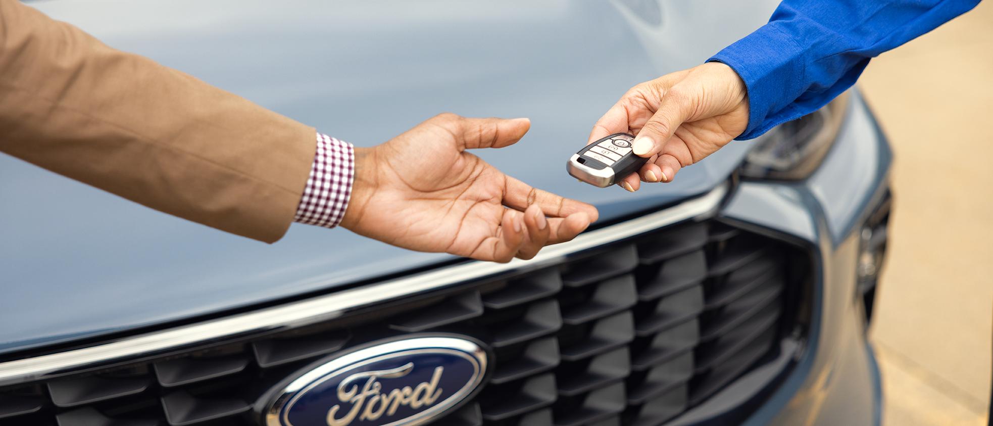 A Ford Service representative hands a key fob over to a Ford owner