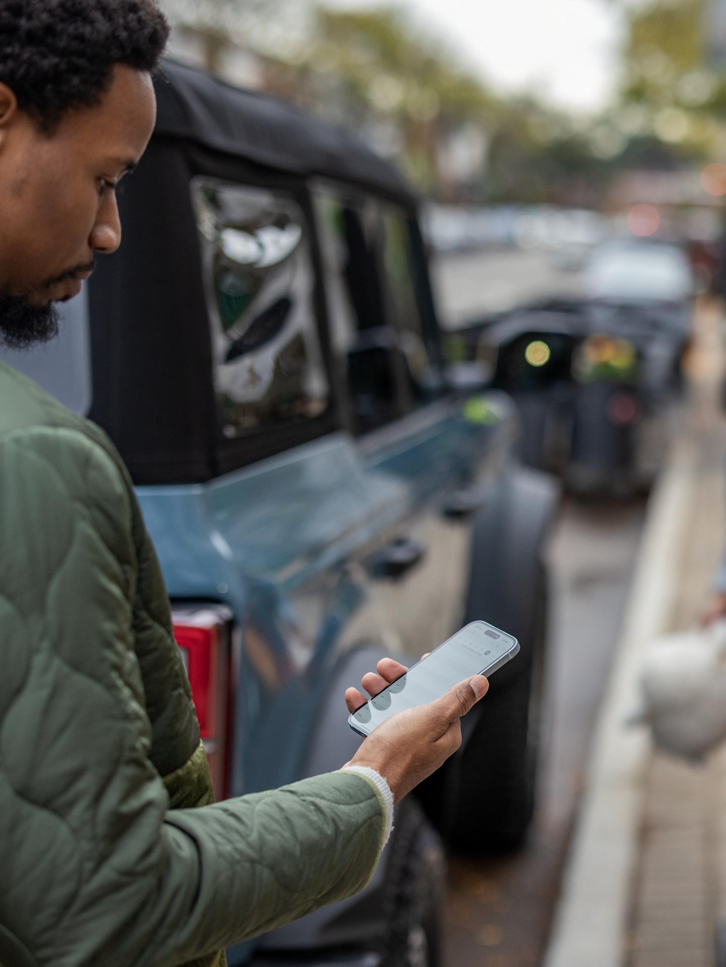 Person standing beside a Ford Bronco using a smartphone.